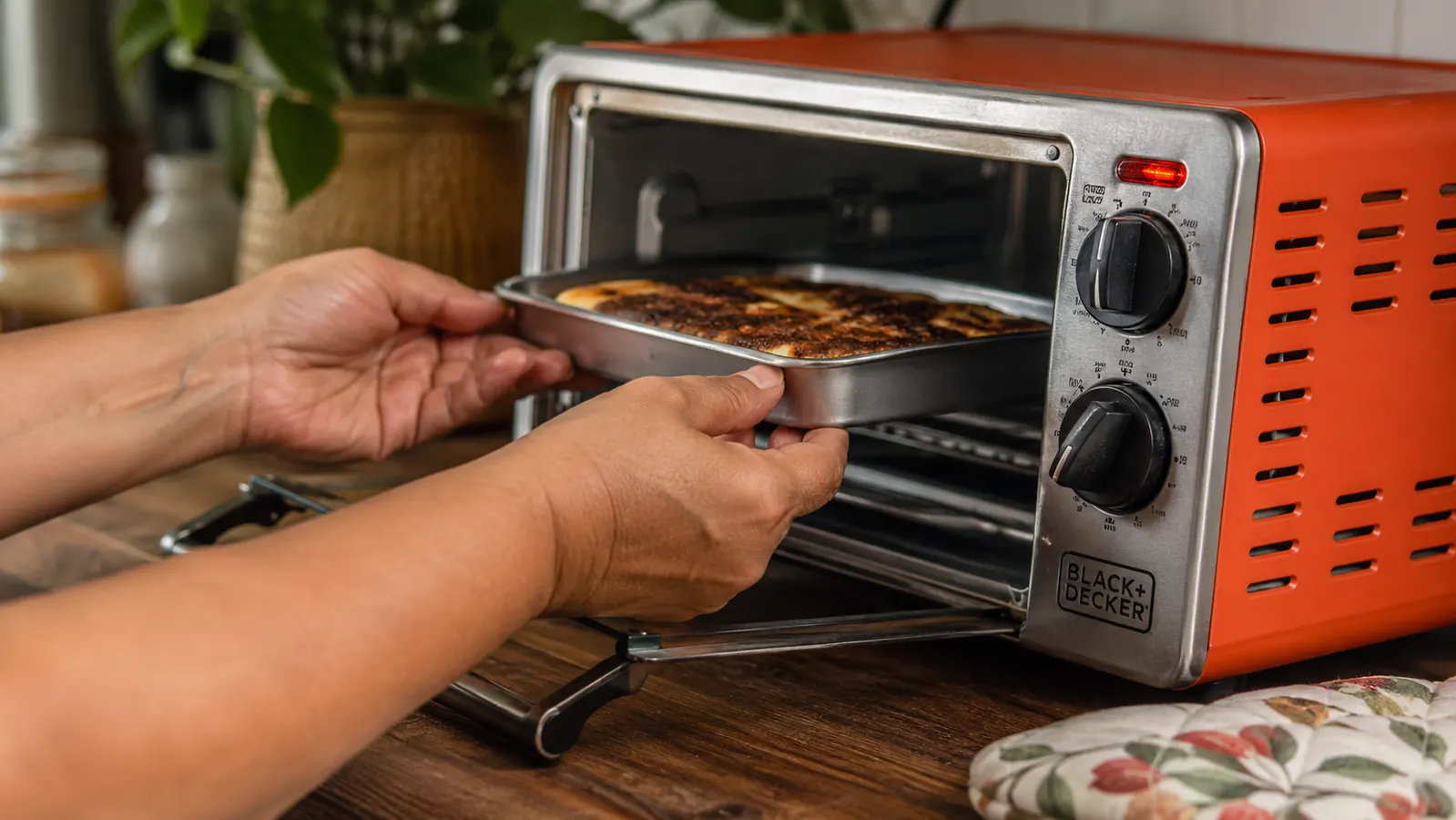 Hand sliding a small baking pan with two pieces of toast into a compact toaster oven