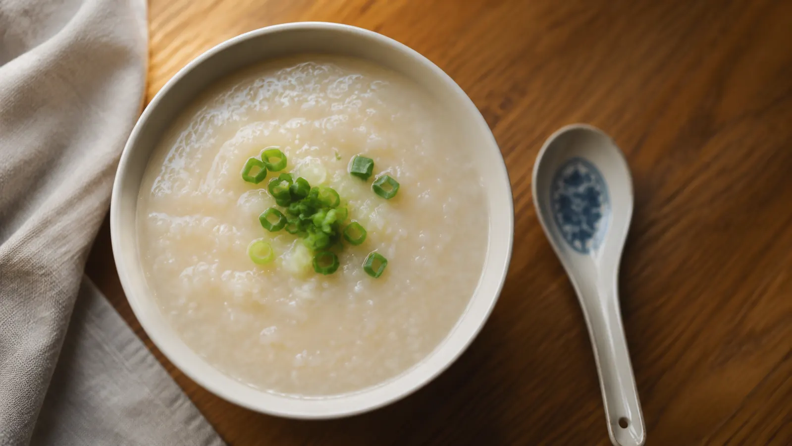 Bowl of soft congee made in the Aroma rice cooker, garnished with sliced green onion, set on a small wooden table