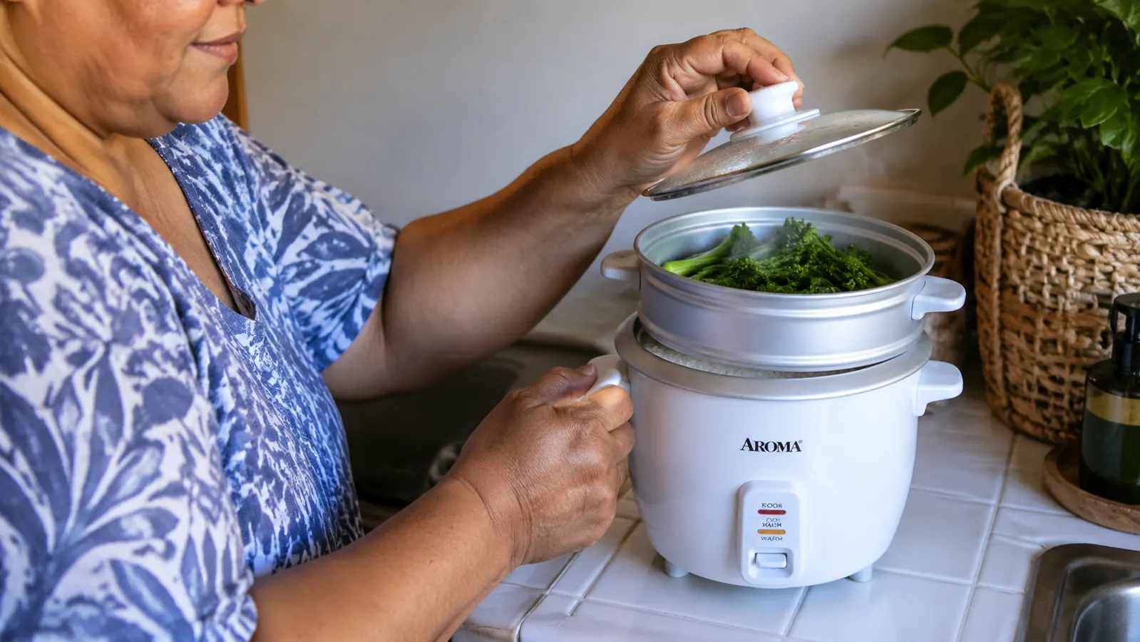 Small steamer tray inside an Aroma rice cooker holding broccoli florets above cooking rice