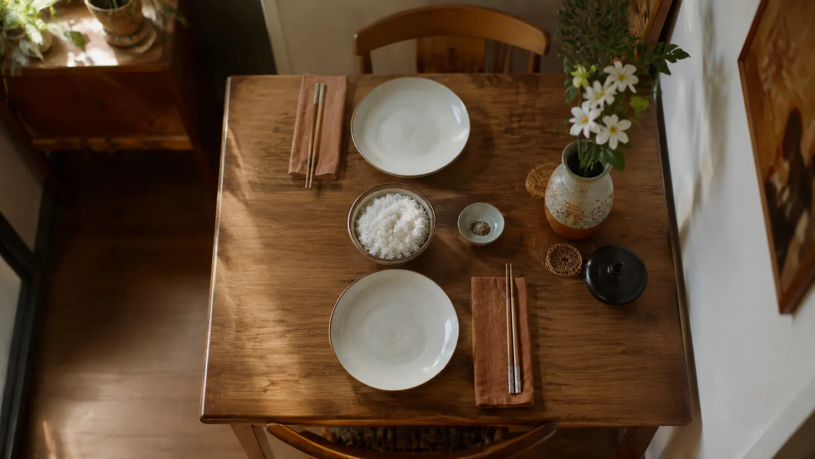 A bowl of perfectly cooked white rice next to a folded dish towel on a small kitchen table set for two