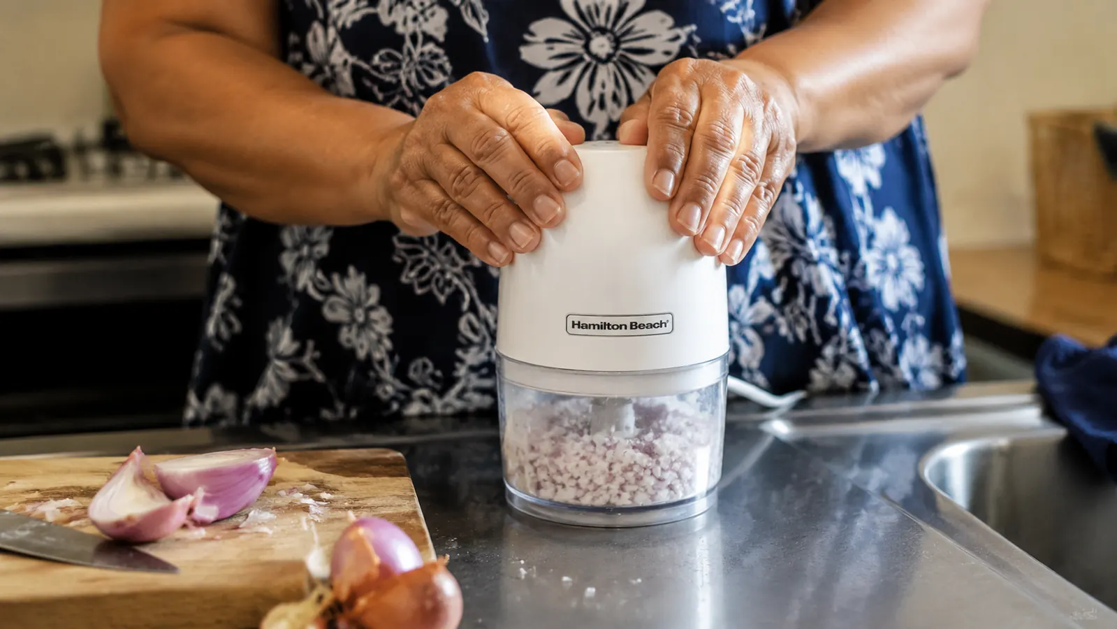 Hands pressing the lid of the Hamilton Beach food chopper to pulse-chop onions inside the clear 3-cup bowl