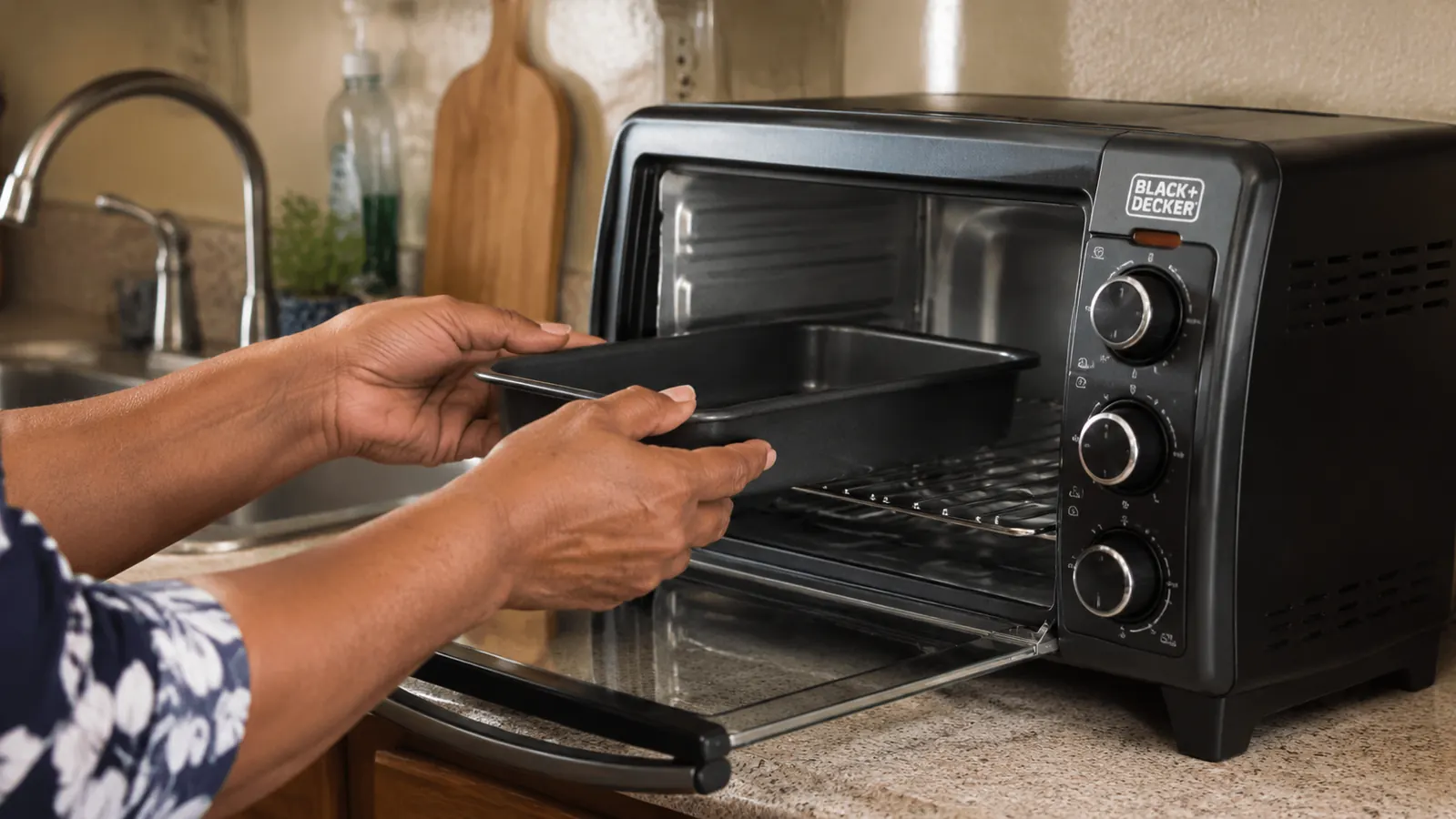 Hands placing a small 6-inch baking pan into the toaster oven rack