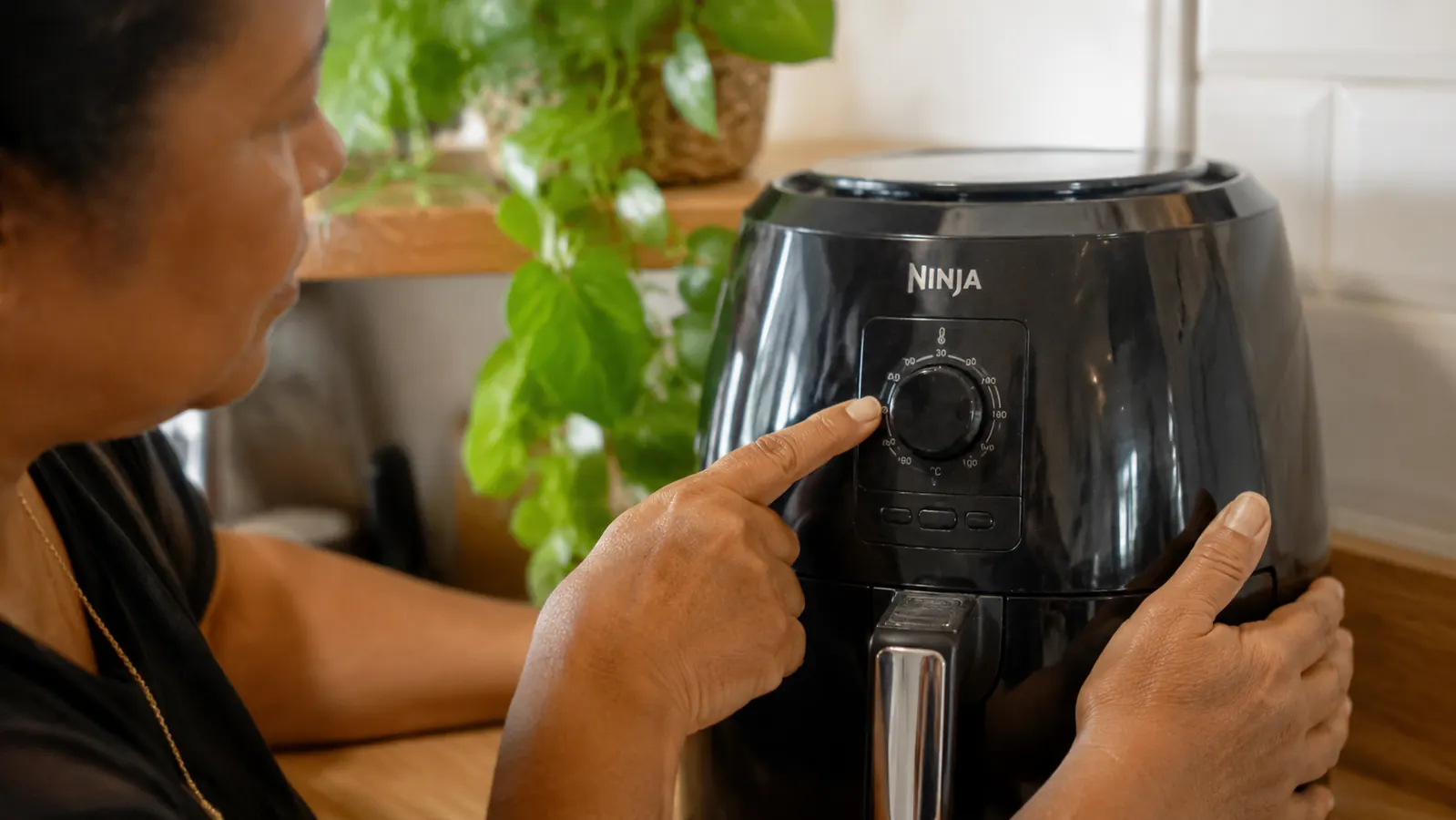Hand pointing at the temperature dial on the Ninja air fryer showing a setting between 350 and 400 degrees