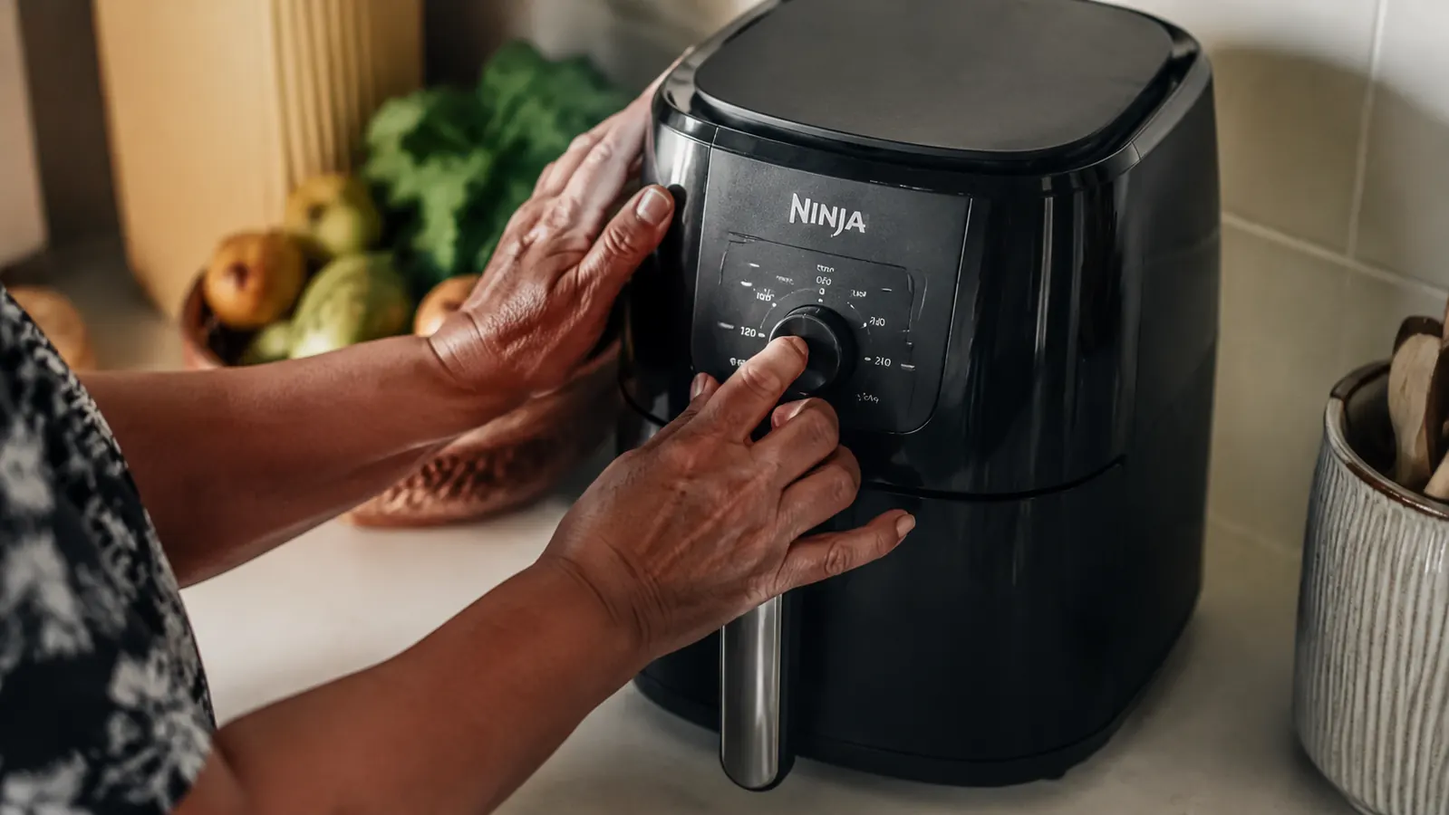 Hand pressing the single dial on the Ninja AF101 air fryer basket drawer sitting on a white countertop